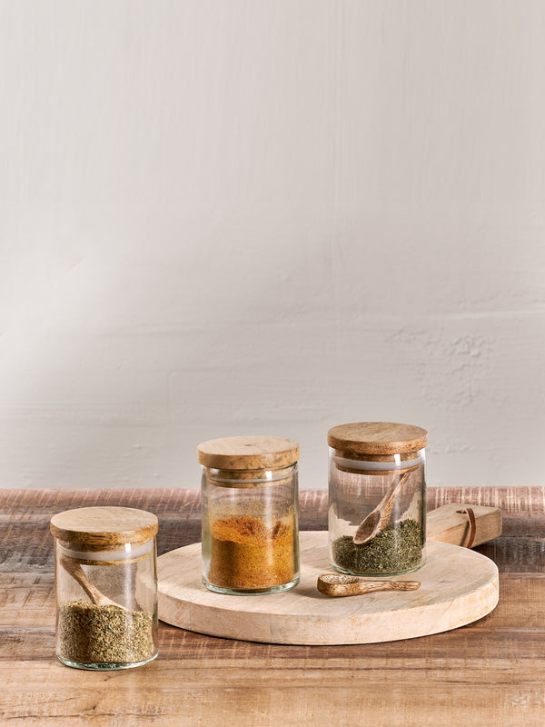 Small storage jars holding spices in a mooJars holding y background, rustic worktop, wooden spoons, on top of a wooden chopping board. 