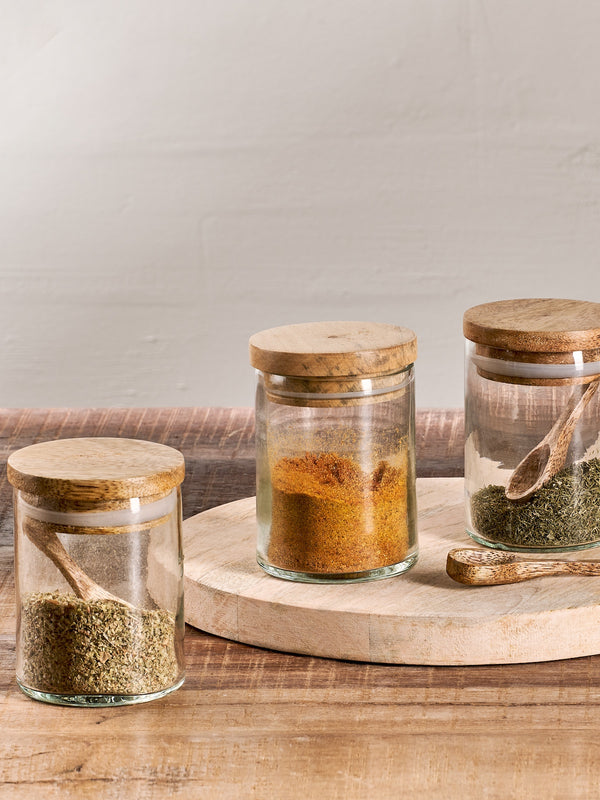 Small storage jars holding spices in a mooJars holding y background, rustic worktop, wooden spoons, on top of a wooden chopping board. 