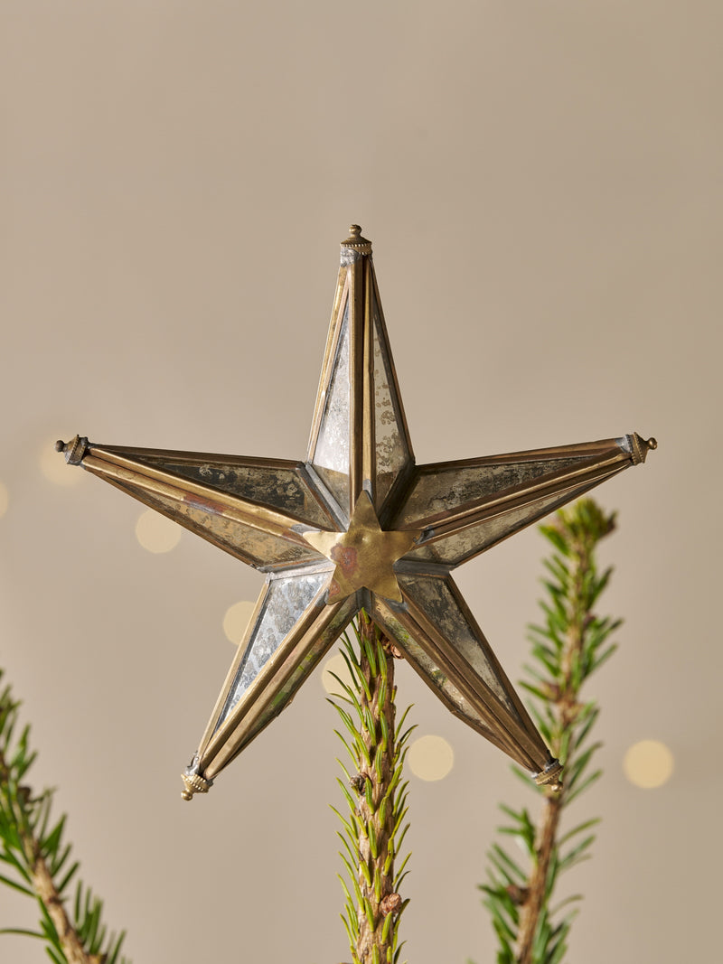 Decorative brass star tree topper with mirrored glass ornament on a Christmas tree with a neutral background