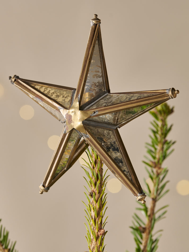 Decorative brass star tree topper with mirrored glass ornament on a Christmas tree with a neutral background