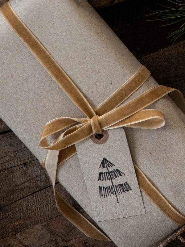 Gift wrapped in brown paper with a beige ribbon by THATCH Living and a tag on a wooden surface