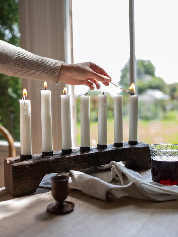 Person lighting candles on a wooden candle holder from THATCH Living with a glass of red wine in the background.