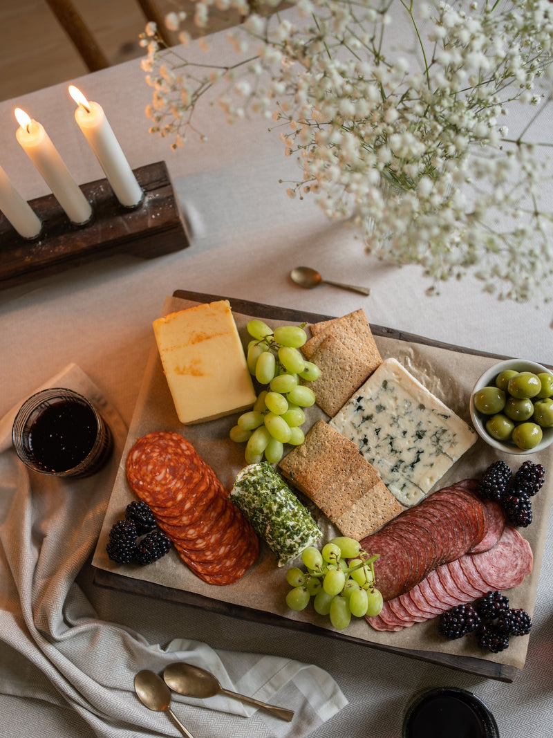 Platter of assorted cheeses, meats, and fruits with candles and flowers on a table.