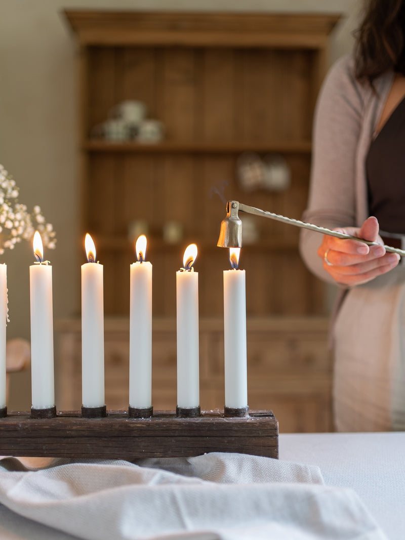 Wooden Candle holder from THATCH Living with lit candles on a table, person lighting another candle in the background.