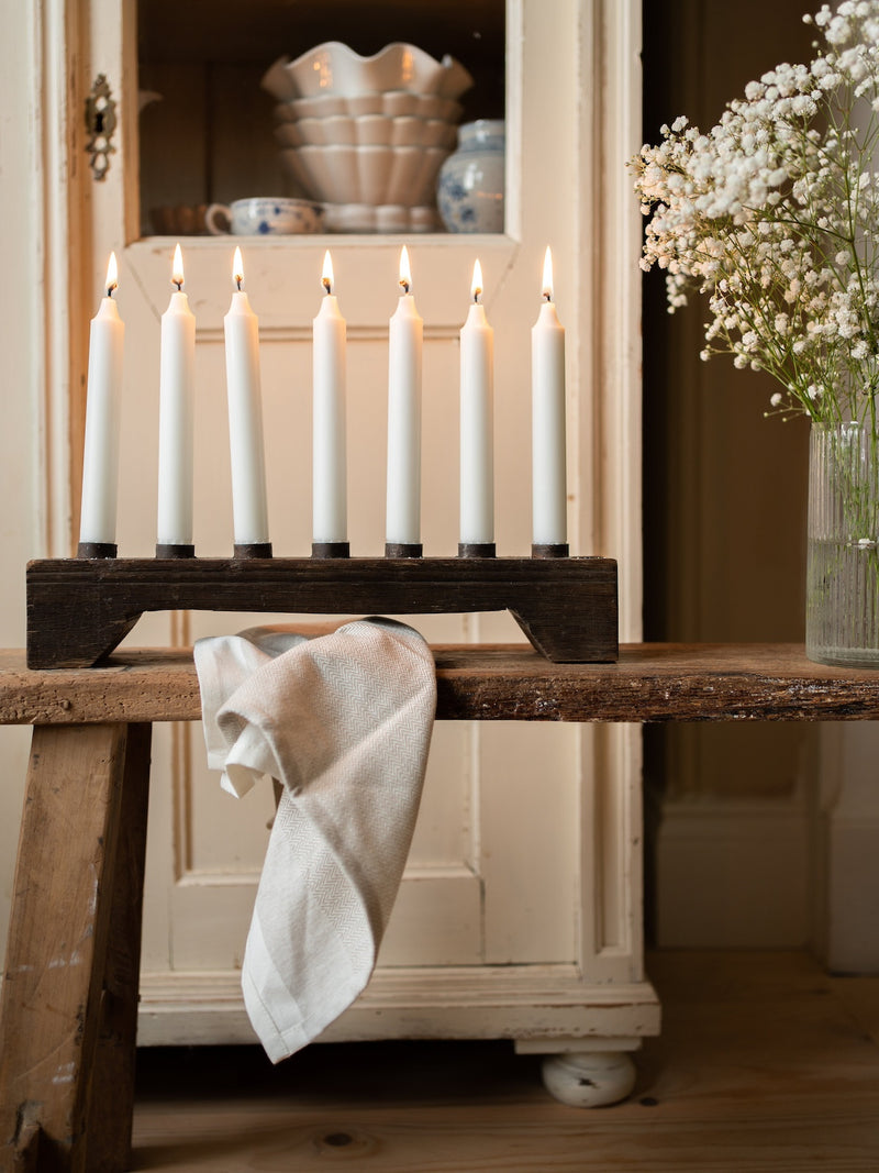 Candles on a wooden candle holder stand with a rustic from THATCH Living cabinet and flowers in the background