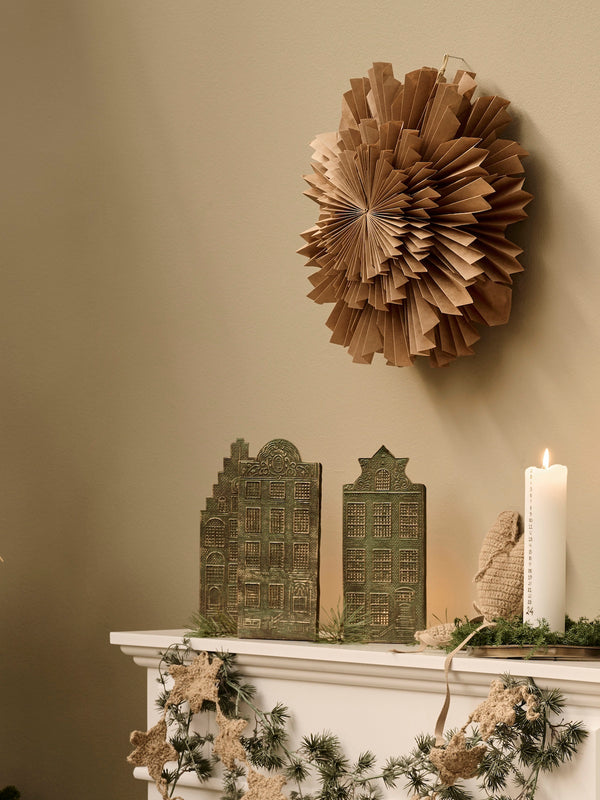 Decorative mantel with paper sunburst, decorative candle holders by THATCH Living shaped like Canal houses, and architectural models against a beige wall. 