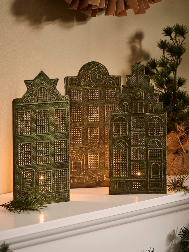 Decorative mantel with paper sunburst, decorative candle holders by THATCH Living shaped like Canal houses, and architectural models against a beige wall. 