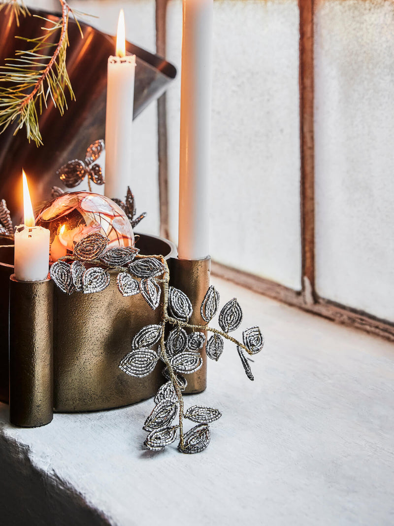Candle holder with white candles on window sill with brass and silver ornament moody vibe.