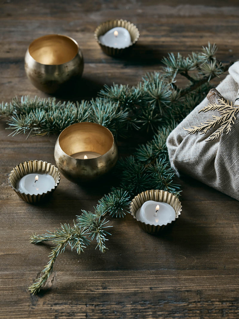 Several Gold and brass decorative tealight holders in a festive setting, rustic table, greenery and presents.