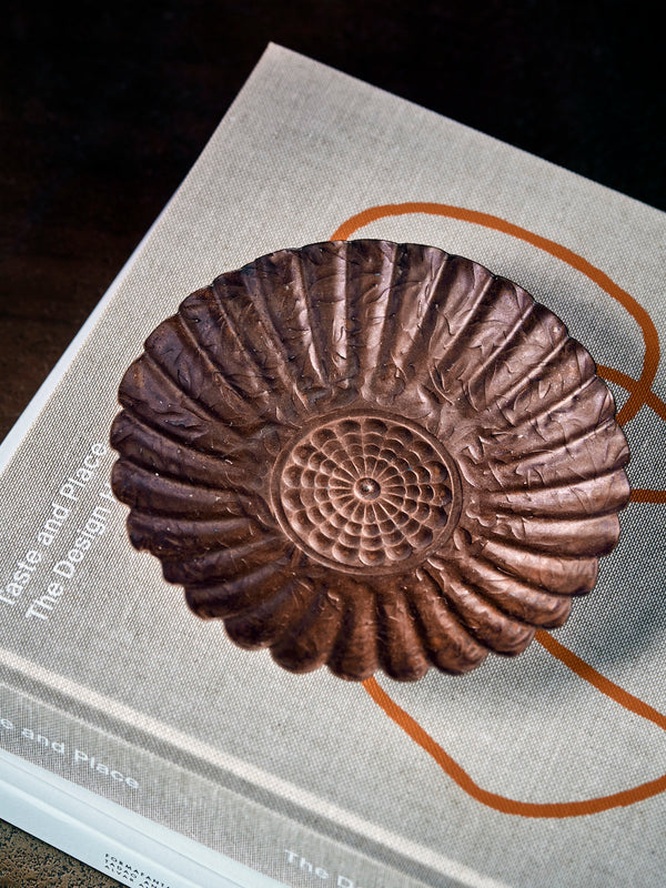HDFofo brown decorative tray metal plate with scalloped edges on top of books on a rustic table and setting.