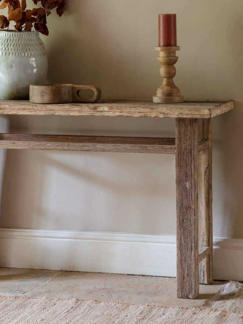 Wooden console table with a candle and decorative items against a beige wall.
