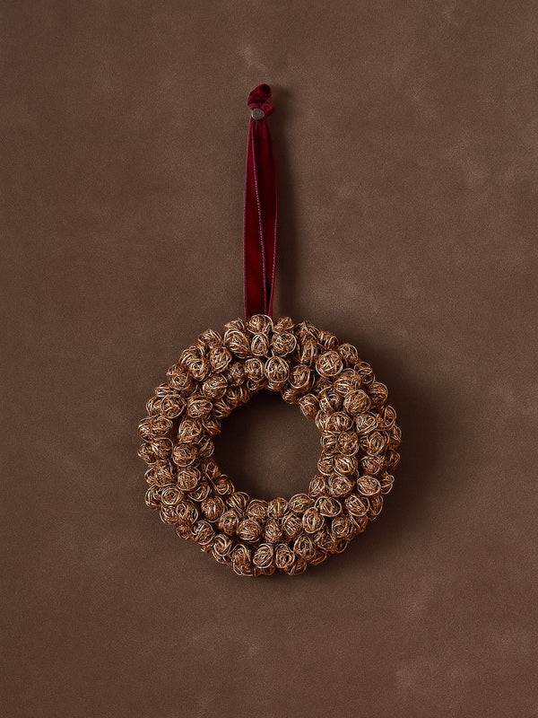 Decorative metal gold antique brass wreath by THATCH Living with a red velvet ribbon on a brown background
