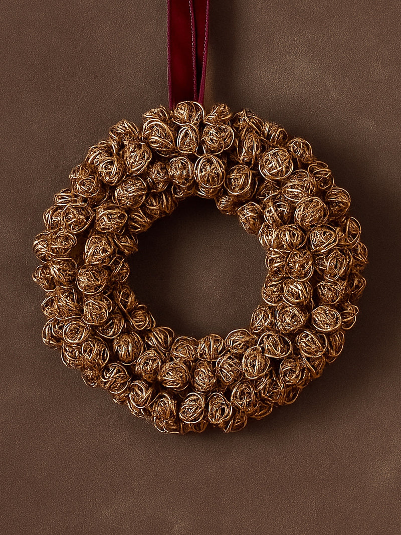 Decorative metal gold antique brass wreath by THATCH Living with a red velvet ribbon on a brown background