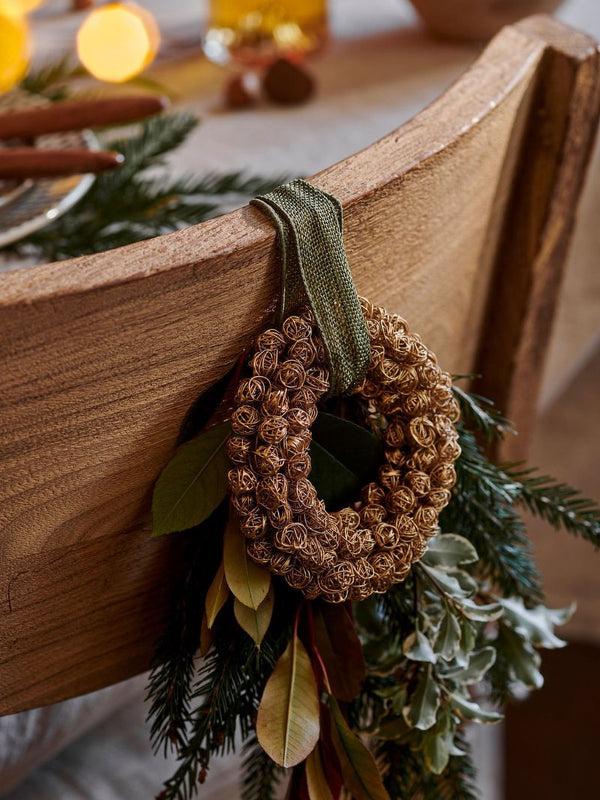 Decorative antique brass metal wreath by THATCH Living with pinecones on a wooden surface with greenery