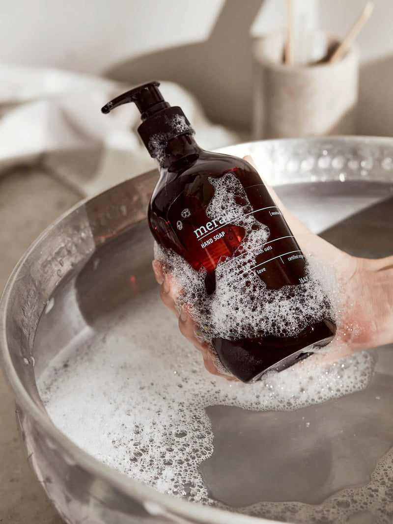 Brown bottle of hand soap being held by hand over a sink.