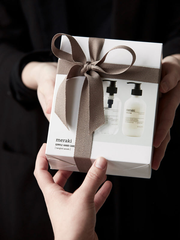 Hands holding and passing a gift set box with brown bow.