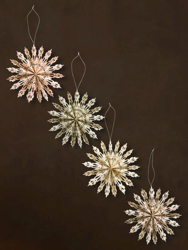 Four recycled paper decorative snowflake ornaments by THATCH Living on a dark background