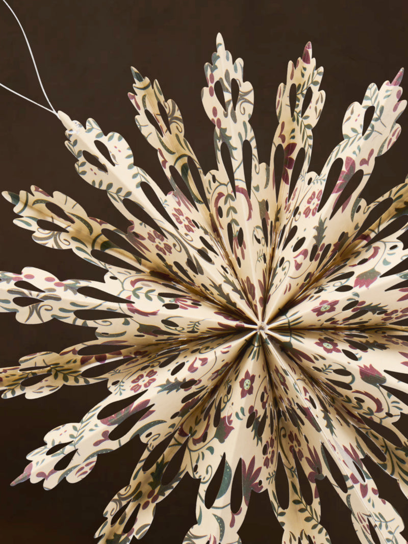 A close-up of a recycled paper decorative snowflake ornament by THATCH Living on a dark background
