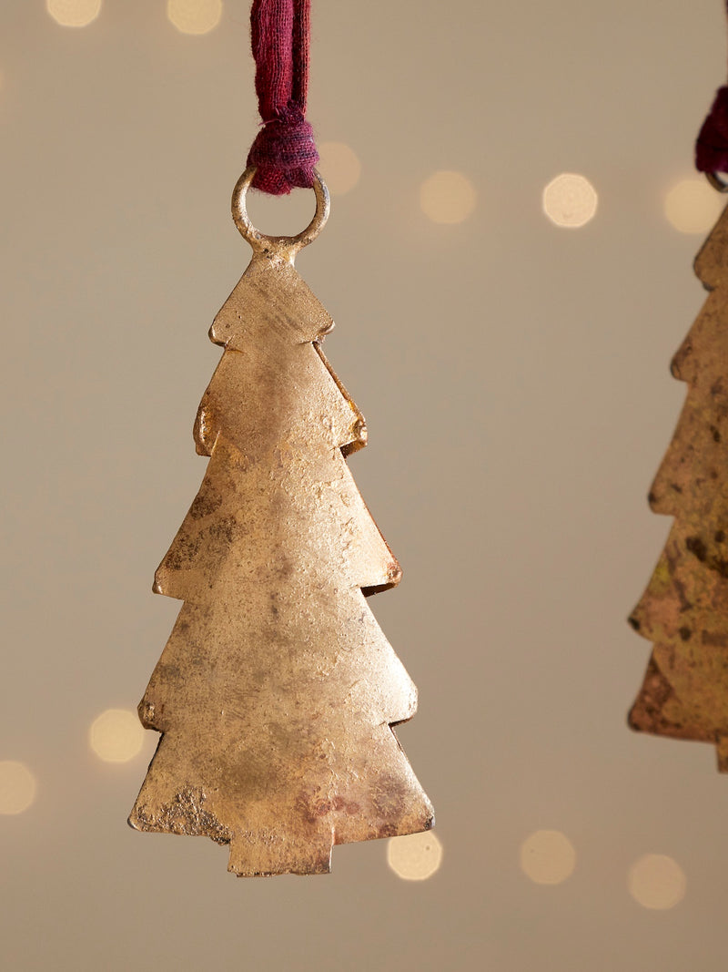Decorative metal Christmas tree ornament by THATCH Living on a beige background with blurred lights.