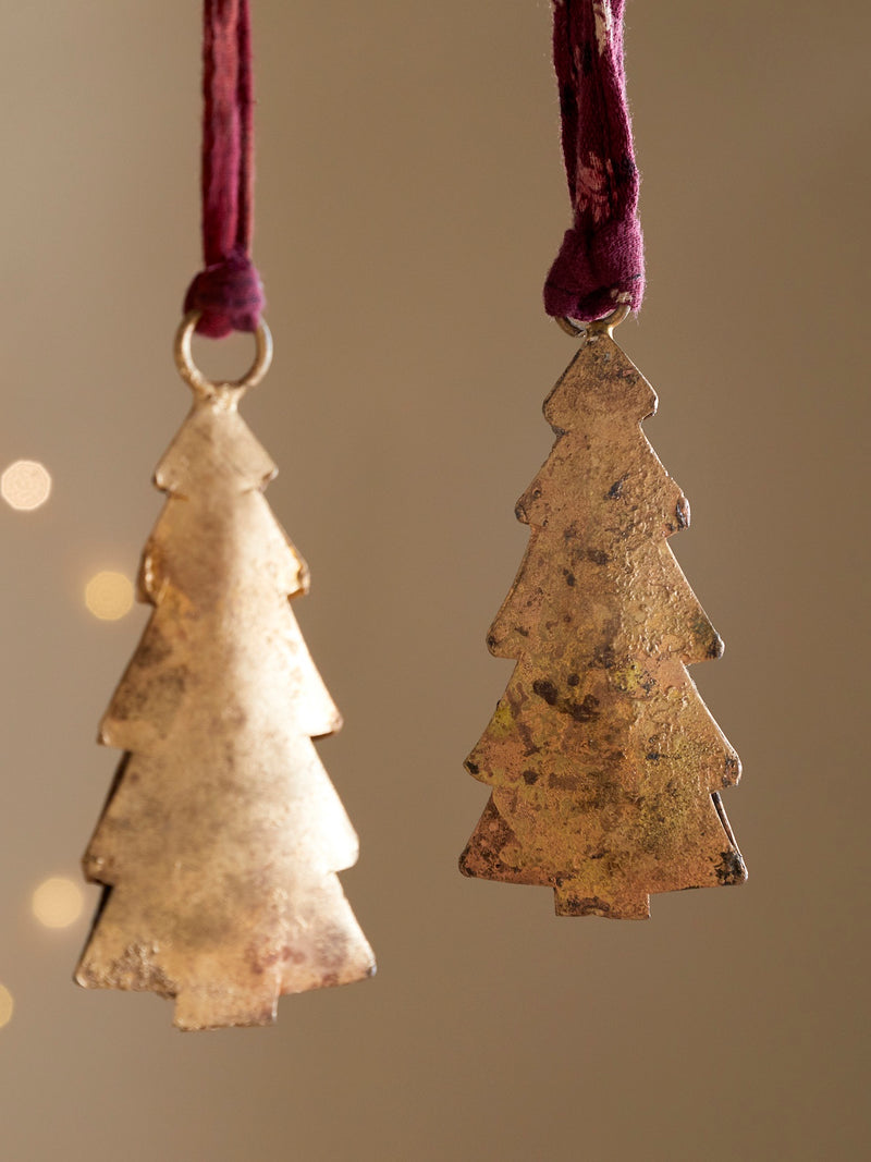 Two tree-shaped rustic metal ornaments by THATCH Living hanging from purple ribbons against a neutral background