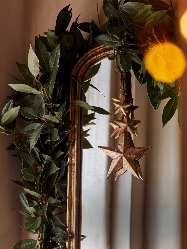 Decorative wreath with green leaves and star-shaped hanging gold ornaments by THATCH Living on a mirror.