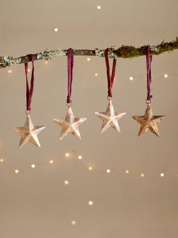 Four rustic star-shaped ornaments by THATCH Living hanging from a branch against a softly lit background