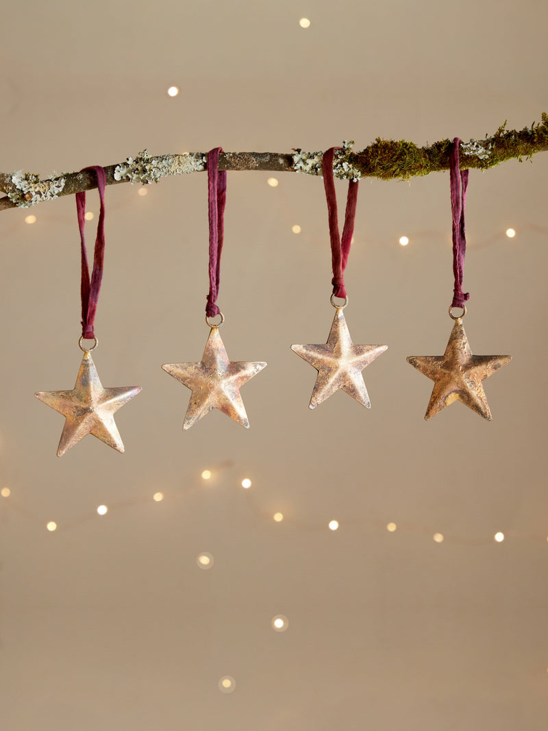 Four rustic star-shaped ornaments by THATCH Living hanging from a branch against a softly lit background