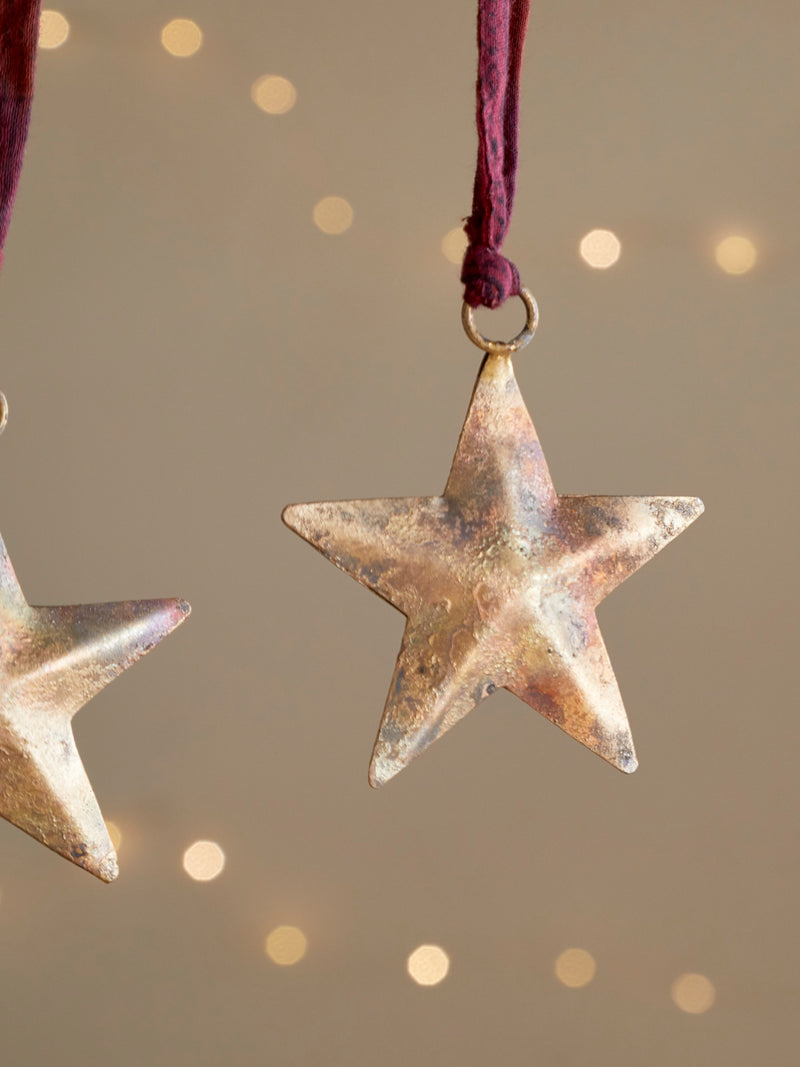 Bronze star-shaped ornament by THATCH Living hanging on a string against a warm, blurred background.