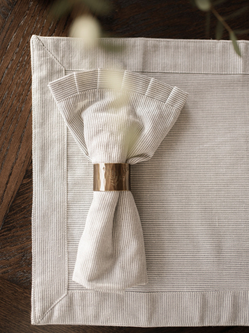Folded napkin with a brass napkin ring on a textured placemat by THATCH Living