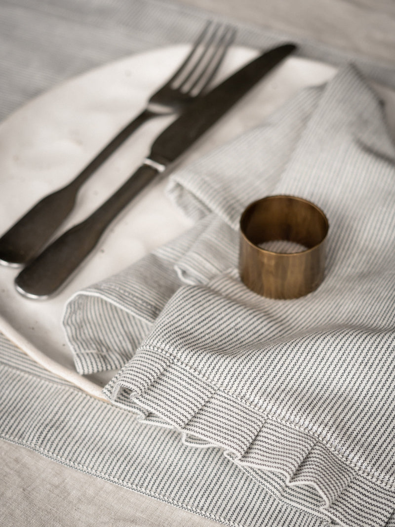 Silverware on a textured gray napkin with a brass napkin ring by THATCH Living