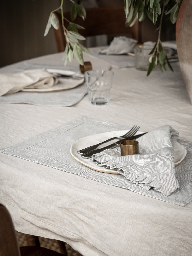 Dining table setting with plates, cutlery, brass napkin ring and glasses on a textured tablecloth by THATCH Living