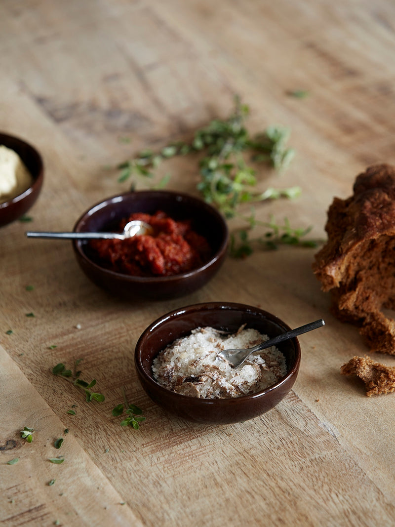 Salt spoon stainless steel in brown serving salt bowl on top of a rustic table with bread, moody vibe.