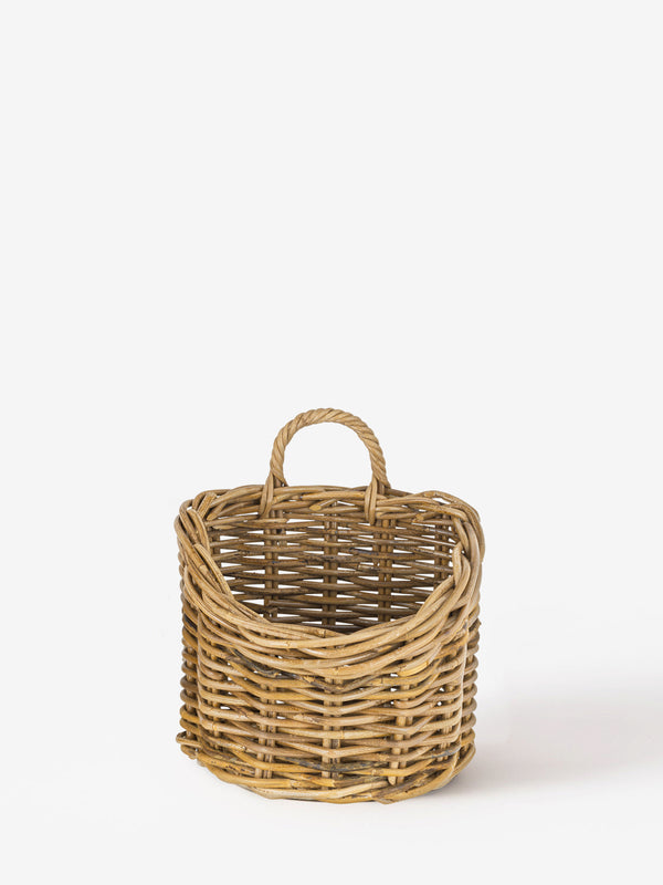 A wicker wall hung basket by THATCH Living with handles on a white background